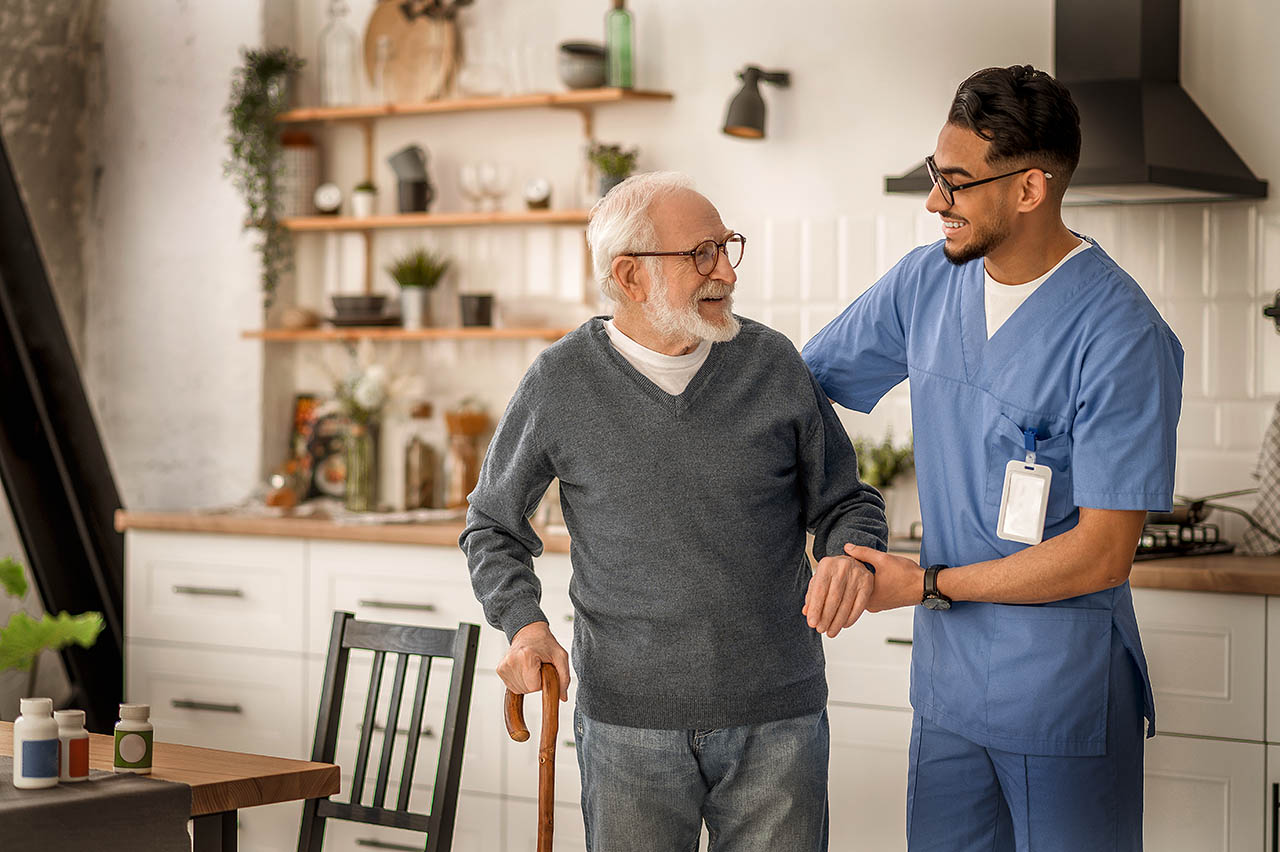 Ein älterer Mann wird von einem Pfleger beim Laufen gestützt.