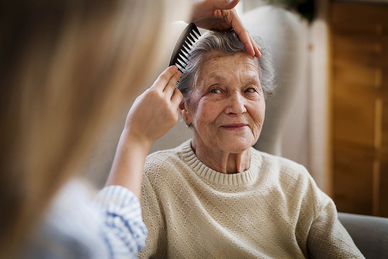 Einer älteren Frau werden ihre Haare von ihrer Enkelin gekämmt.