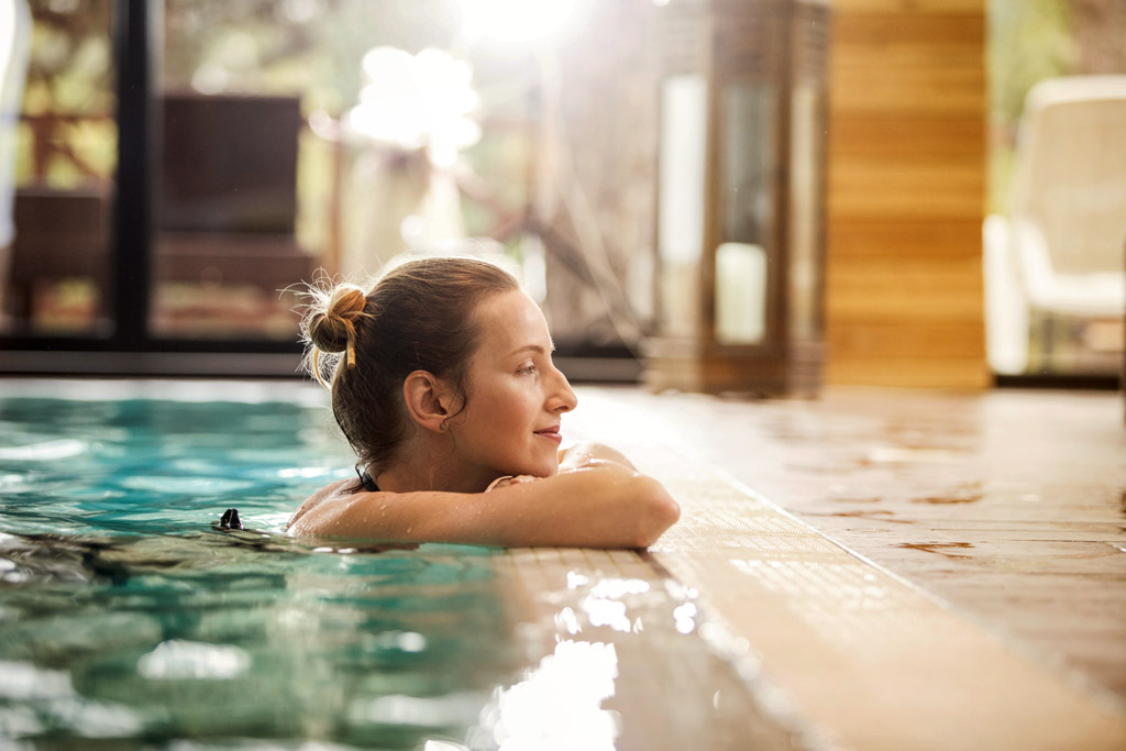 Eine Frau lehnt am Beckenrand eines Schwimmbades.