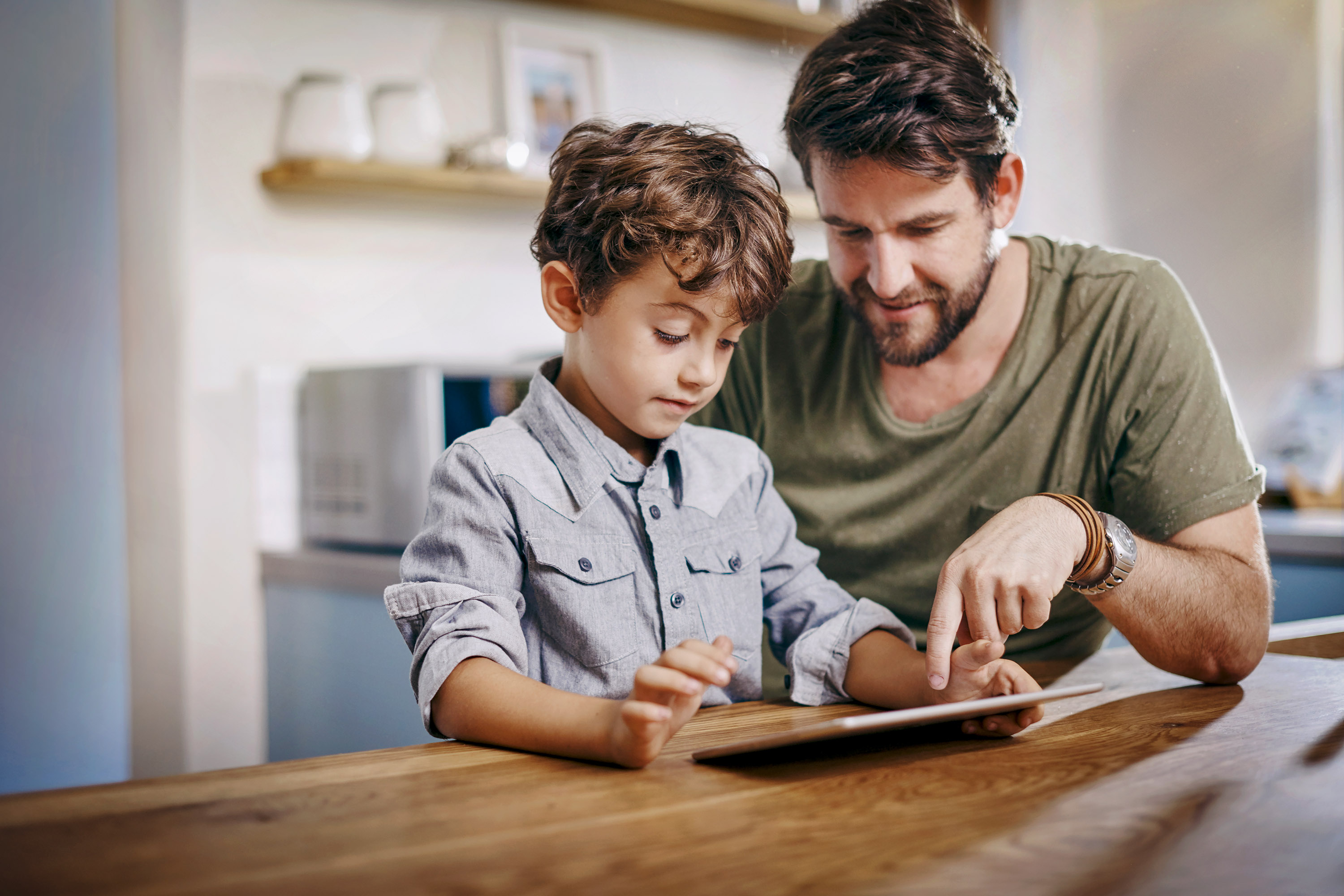 Ein Vater übt mit seinem Sohn die Benutzung des Tablets.