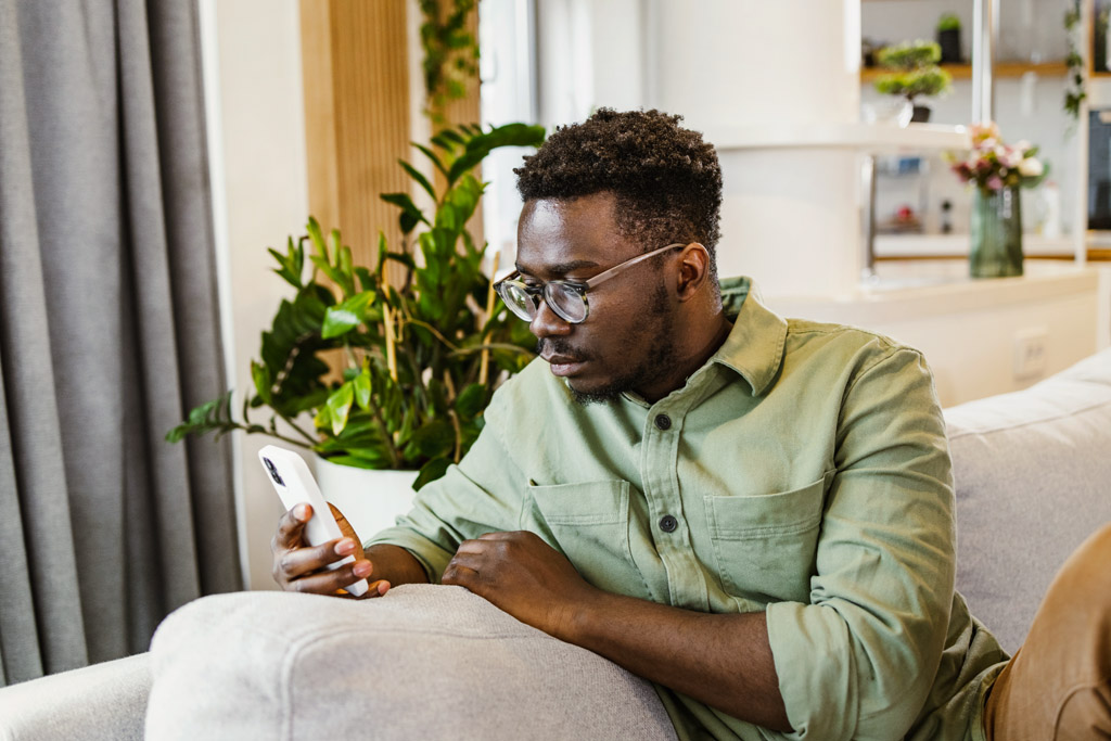 Ein Mann sitzt auf dem Sofa und benutzt sein Mobiltelefon.
