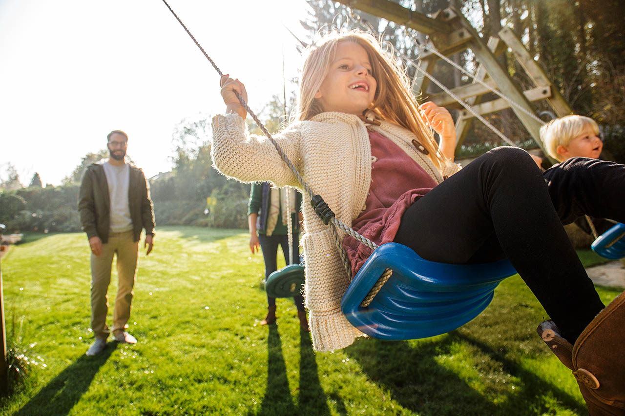 Ein Vater schubst seine Tochter auf der Schaukel im Garten an.