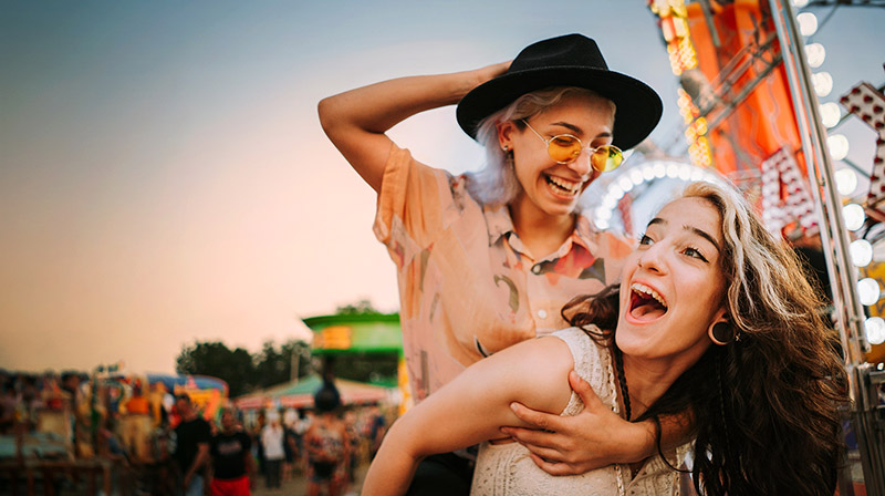 Zwei junge Frauen sind auf einem Festplatz und lachen miteinander.