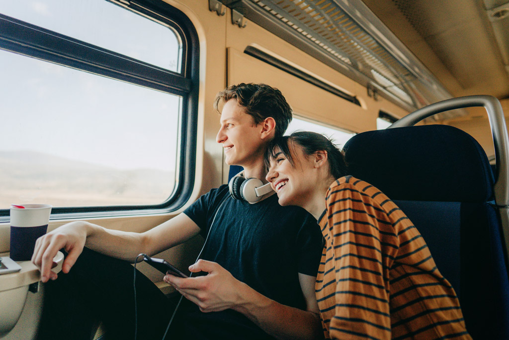 ein junges Paar sitzt gemeinsam im Zug und sie schauen fröhlich aus dem Fenster.