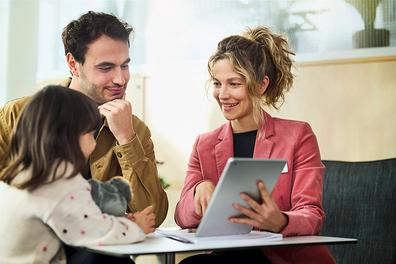 Eine Kundenberaterin berät einen Mann und seine kleine Tochter und zeigt ihnen etwas auf einem Tablet.