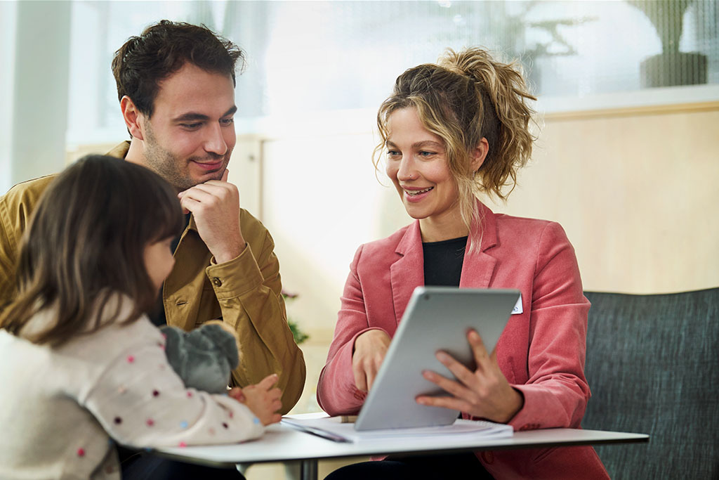 Eine Kundenberaterin berät einen Mann und seine kleine Tochter und zeigt ihnen etwas auf einem Tablet.