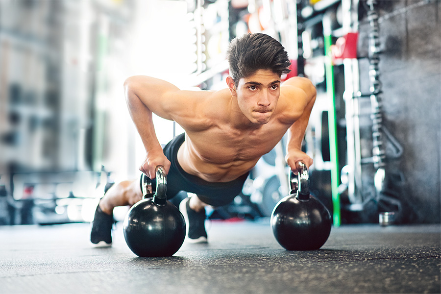 Junger Mann im Fitnessraum macht Push auf Kettleballs.