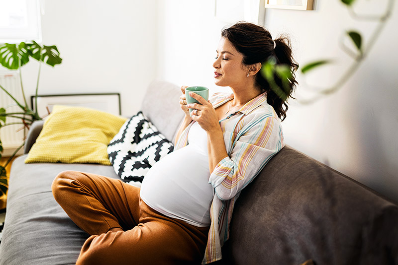 Schwangere Frau sitzt auf Sofa.